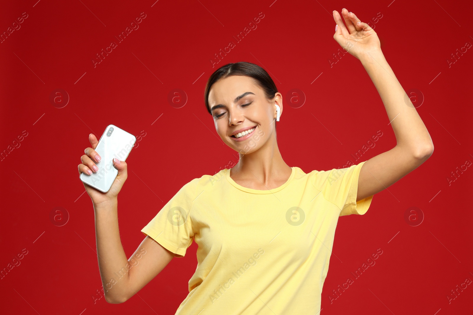 Photo of Happy young woman with smartphone listening to music through wireless earphones on red background