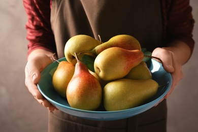 Photo of Woman holding plate with ripe pears on grey background, closeup