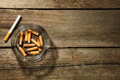 Photo of Glass ashtray with cigarette stubs on wooden table, flat lay. Space for text