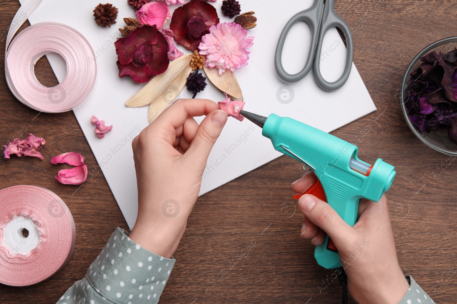 Photo of Woman using hot glue gun to make craft at wooden table, top view