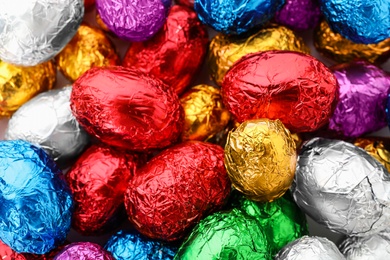 Many chocolate eggs wrapped in bright foil as background, closeup view