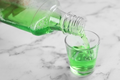 Photo of Pouring mouthwash in glass on marble background, closeup. Teeth care