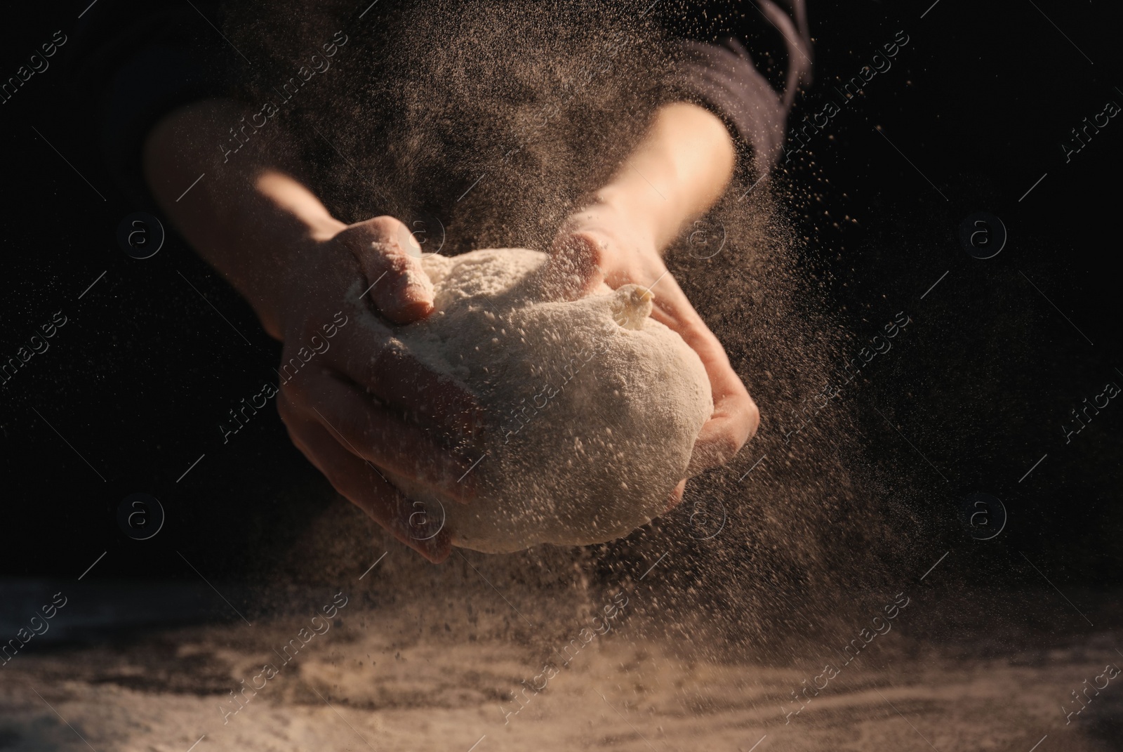 Photo of Making bread. Woman kneading dough at table on dark background, closeup