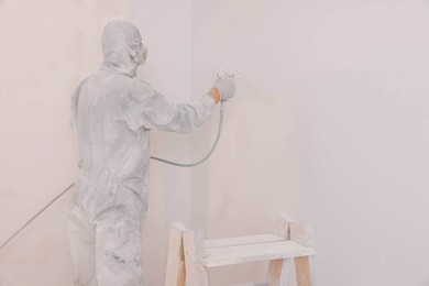 Photo of Decorator in uniform painting wall with sprayer indoors