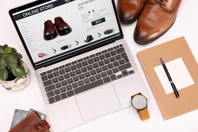 Photo of Online store website on laptop screen. Computer, stationery, credit cards, men's shoes and accessories on white background, above view