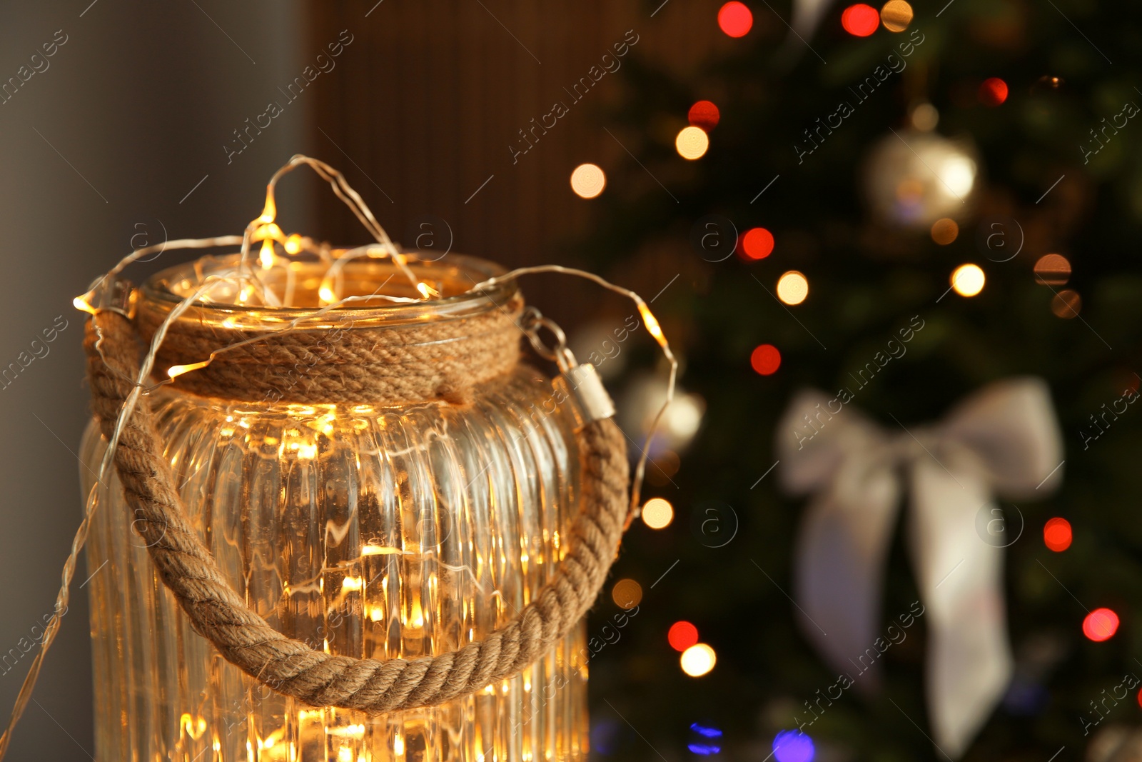 Photo of Jar with shiny lights and blurred Christmas tree on background