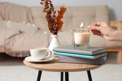 Woman lighting candle at coffee table in room, closeup. Cozy interior