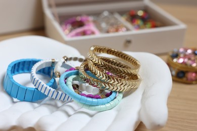 Photo of Ceramic hand stand with many different bracelets on wooden table, closeup