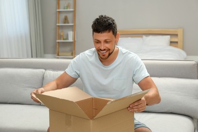 Happy man opening parcel on sofa at home. Internet shopping