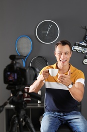 Sport blogger with cup of coffee recording video on camera at home