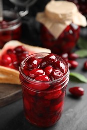 Photo of Delicious dogwood jam with berries in glass jar on black table, closeup