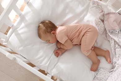 Photo of Cute little baby sleeping in soft crib at home, top view