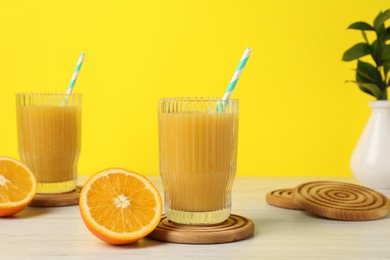 Fresh orange juice and wooden coasters on white wooden table