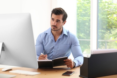 Handsome young man working with notebook and computer at table in office