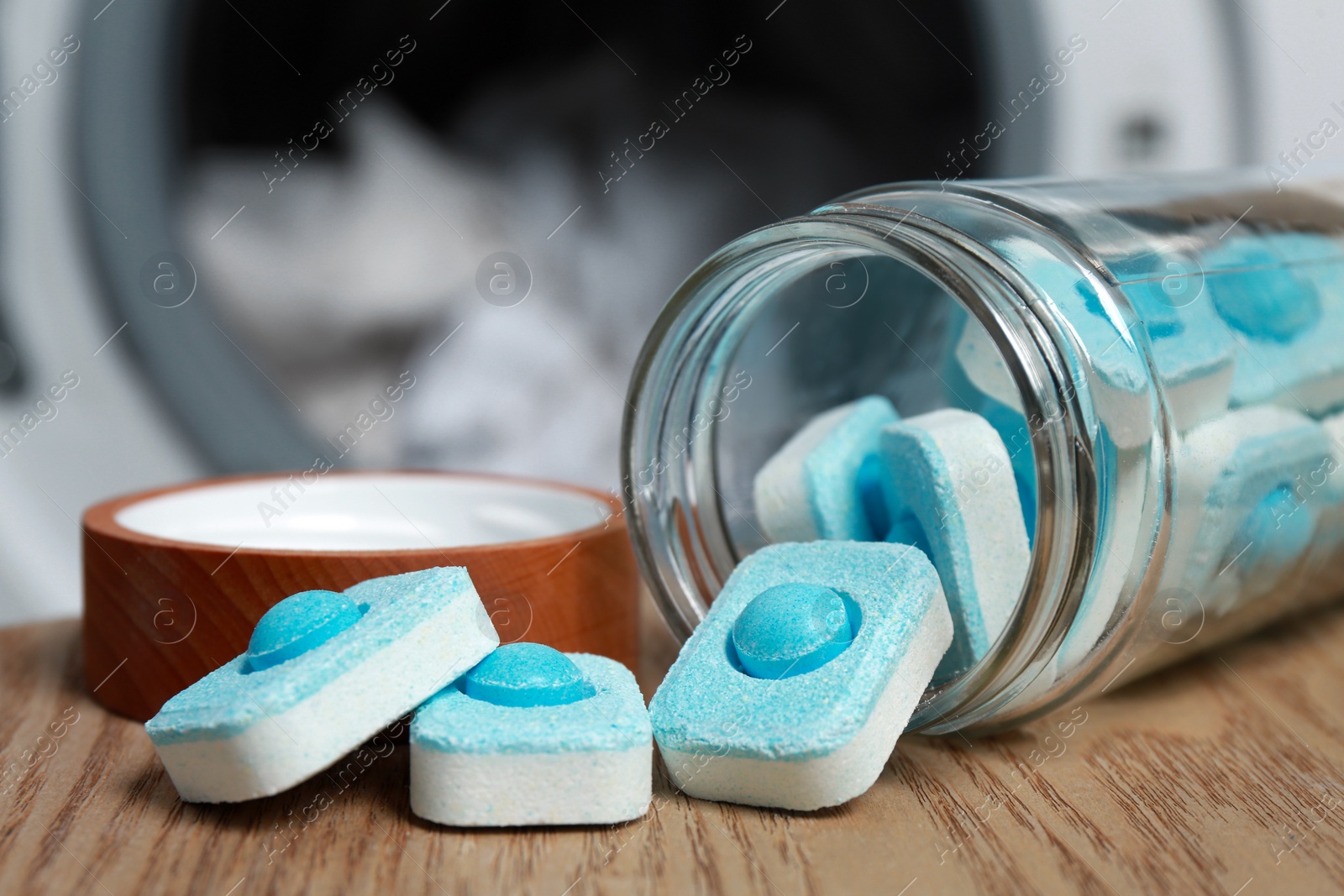 Photo of Jar with water softener tablets on wooden table near washing machine, closeup