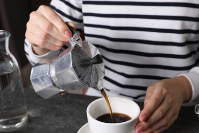 Photo of Woman pouring aromatic coffee from moka pot into cup at grey table indoors, closeup