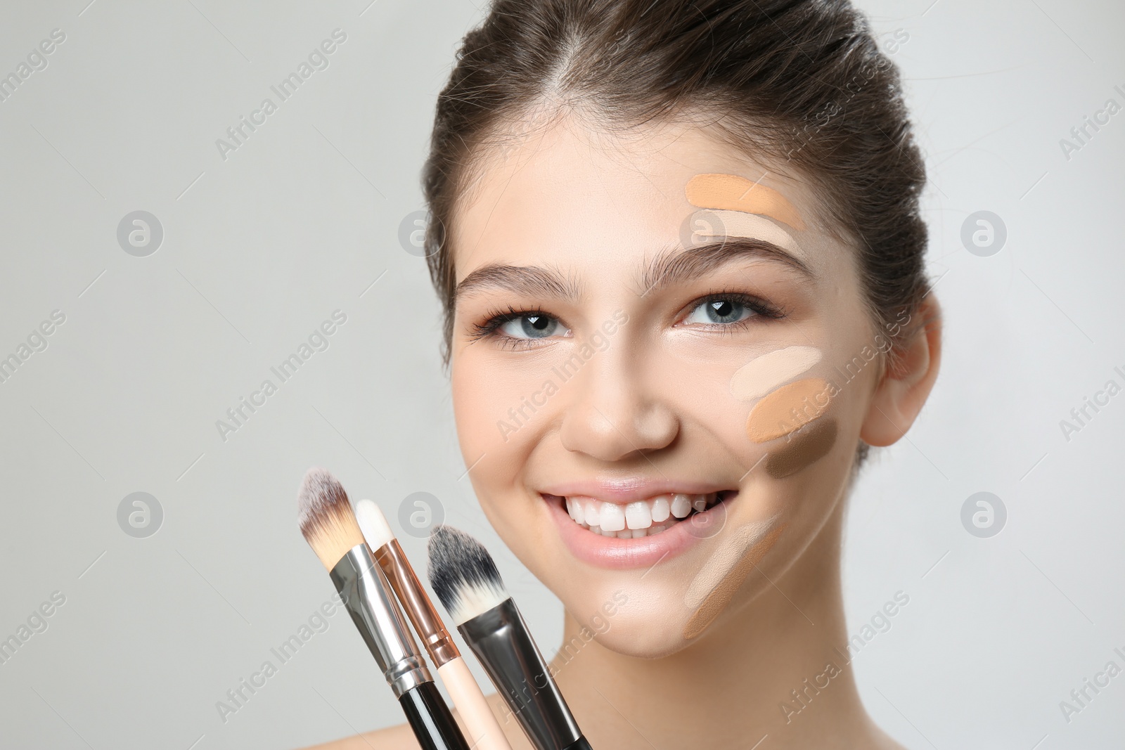 Photo of Beautiful girl with brushes on light grey background. Using concealer and foundation for face contouring