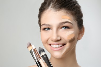 Photo of Beautiful girl with brushes on light grey background. Using concealer and foundation for face contouring