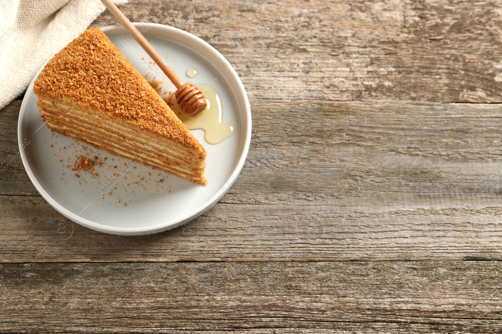 Photo of Slice of delicious layered honey cake served on wooden table, above view. Space for text