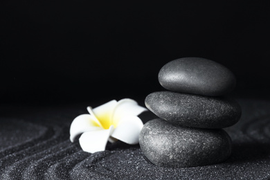 Spa stones and plumeria flower on black sand with beautiful pattern, space for text. Zen concept