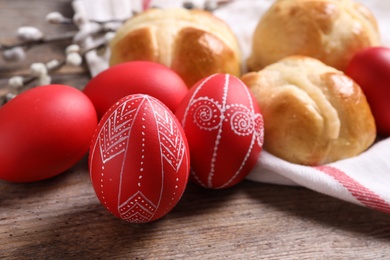 Photo of Red painted Easter eggs and buns on wooden table, closeup