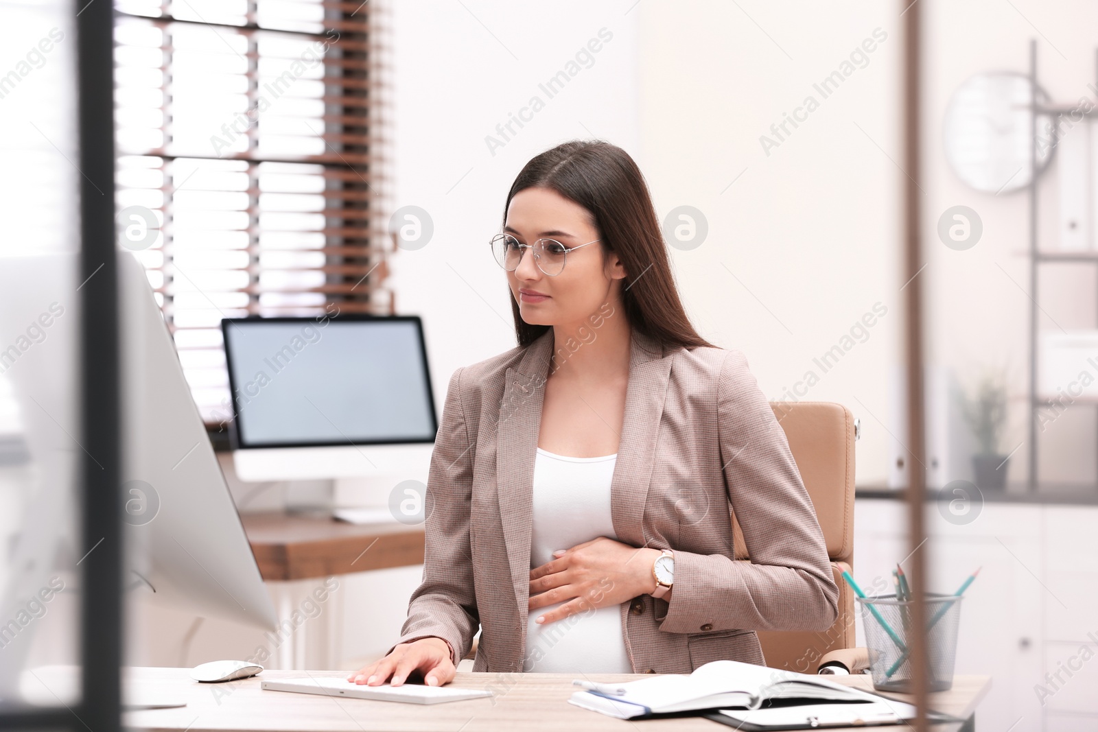 Photo of Young pregnant woman working with computer at table in office