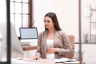 Young pregnant woman working with computer at table in office