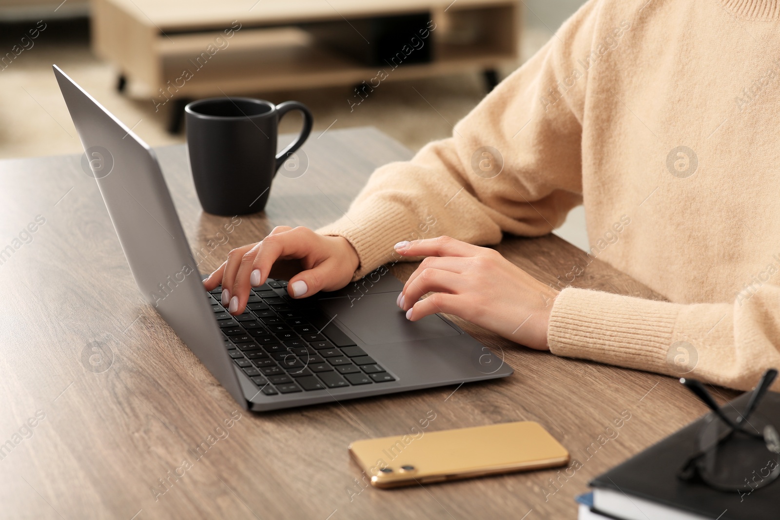 Photo of Woman working with laptop at wooden desk indoors, closeup