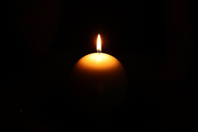 Photo of One round burning candle on black background