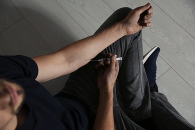 Photo of Male drug addict with syringe sitting on floor, above view