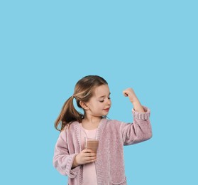 Photo of Cute little child with glass of tasty chocolate milk on light blue background