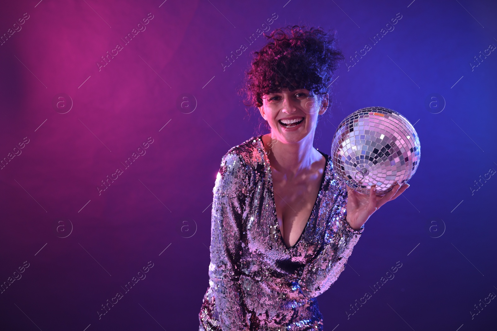 Photo of Beautiful young woman with disco ball posing on color background in neon lights