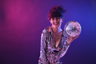 Photo of Beautiful young woman with disco ball posing on color background in neon lights