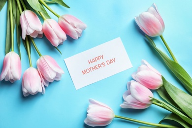 Photo of Beautiful tulips and greeting card with phrase "Happy Mother's Day" on color background