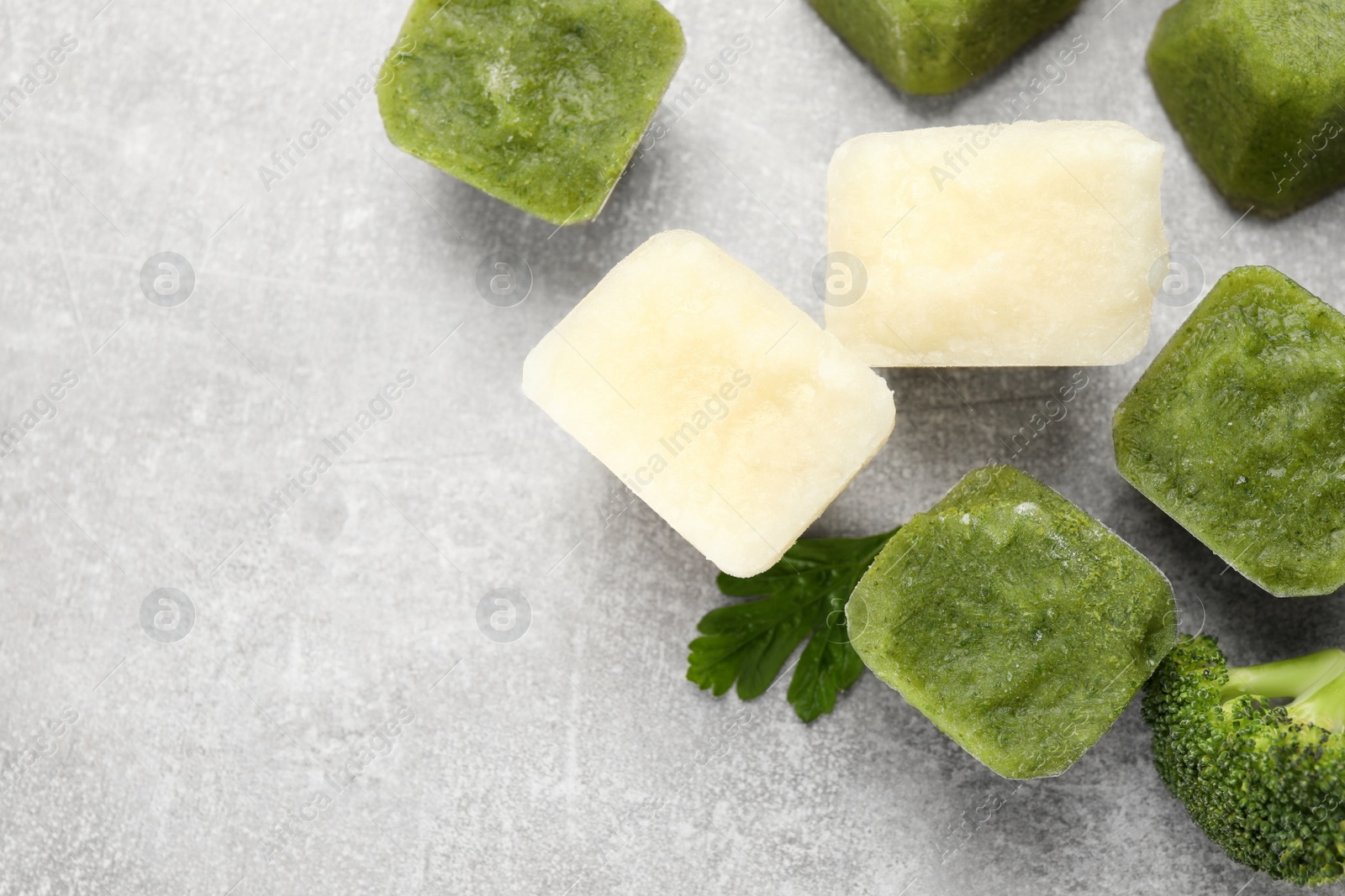 Photo of Frozen cauliflower and broccoli puree cubes on light grey table, flat lay. Space for text
