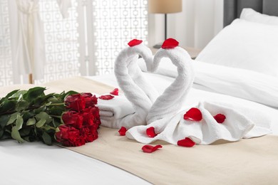 Honeymoon. Swans made of towels and beautiful red roses on bed in room