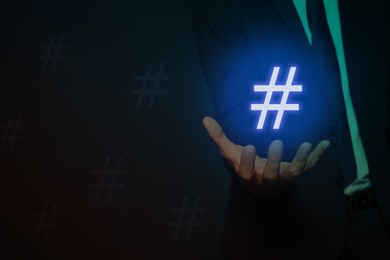 Image of Hashtag concept. Man holding sign on dark background, closeup with space for text