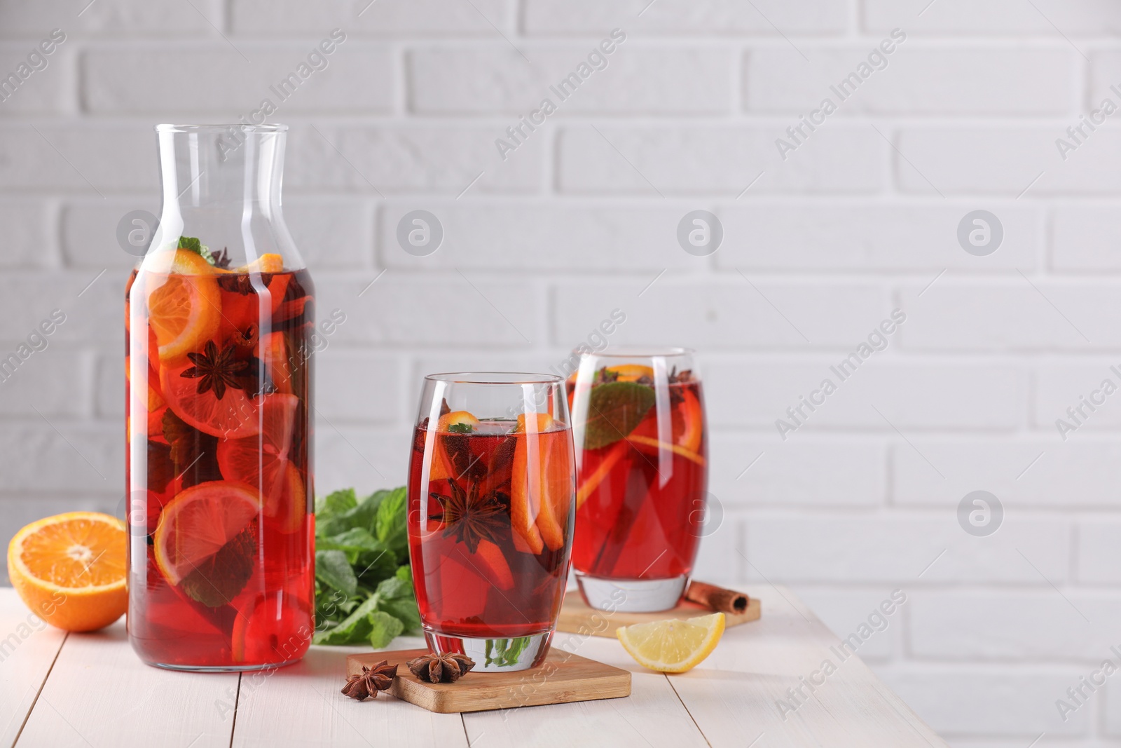 Photo of Delicious punch drink, slices of fruits and anise stars on white wooden table. Space for text