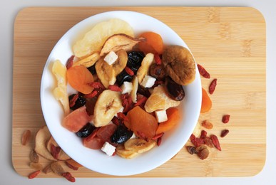 Bowl with different dried fruits on white background, top view