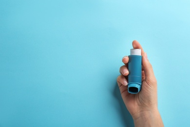 Photo of Woman holding asthma inhaler on color background, top view. Space for text