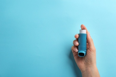 Woman holding asthma inhaler on color background, top view. Space for text