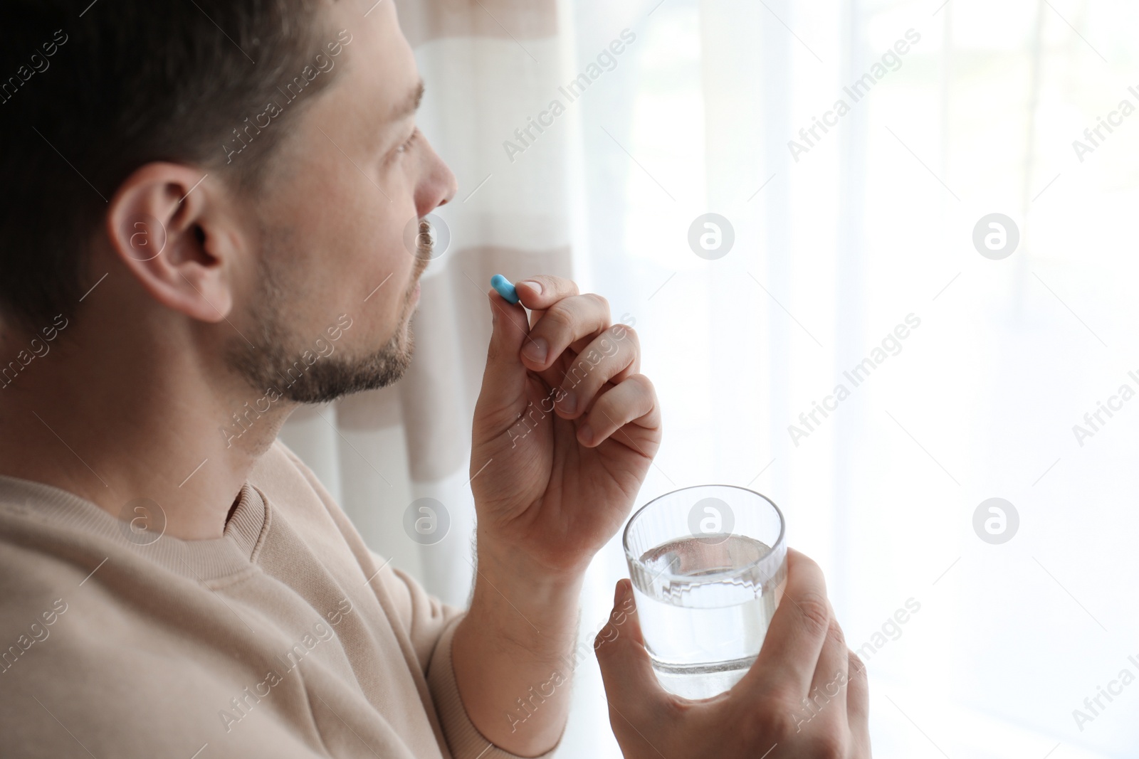 Photo of Man with glass of water taking pill at home