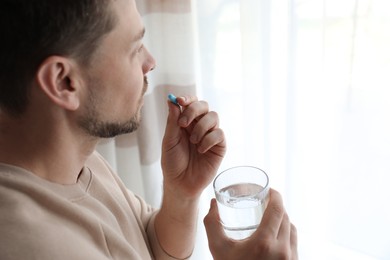 Man with glass of water taking pill at home