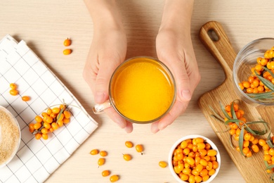 Photo of Woman holding cup with sea buckthorn tea at wooden table, top view