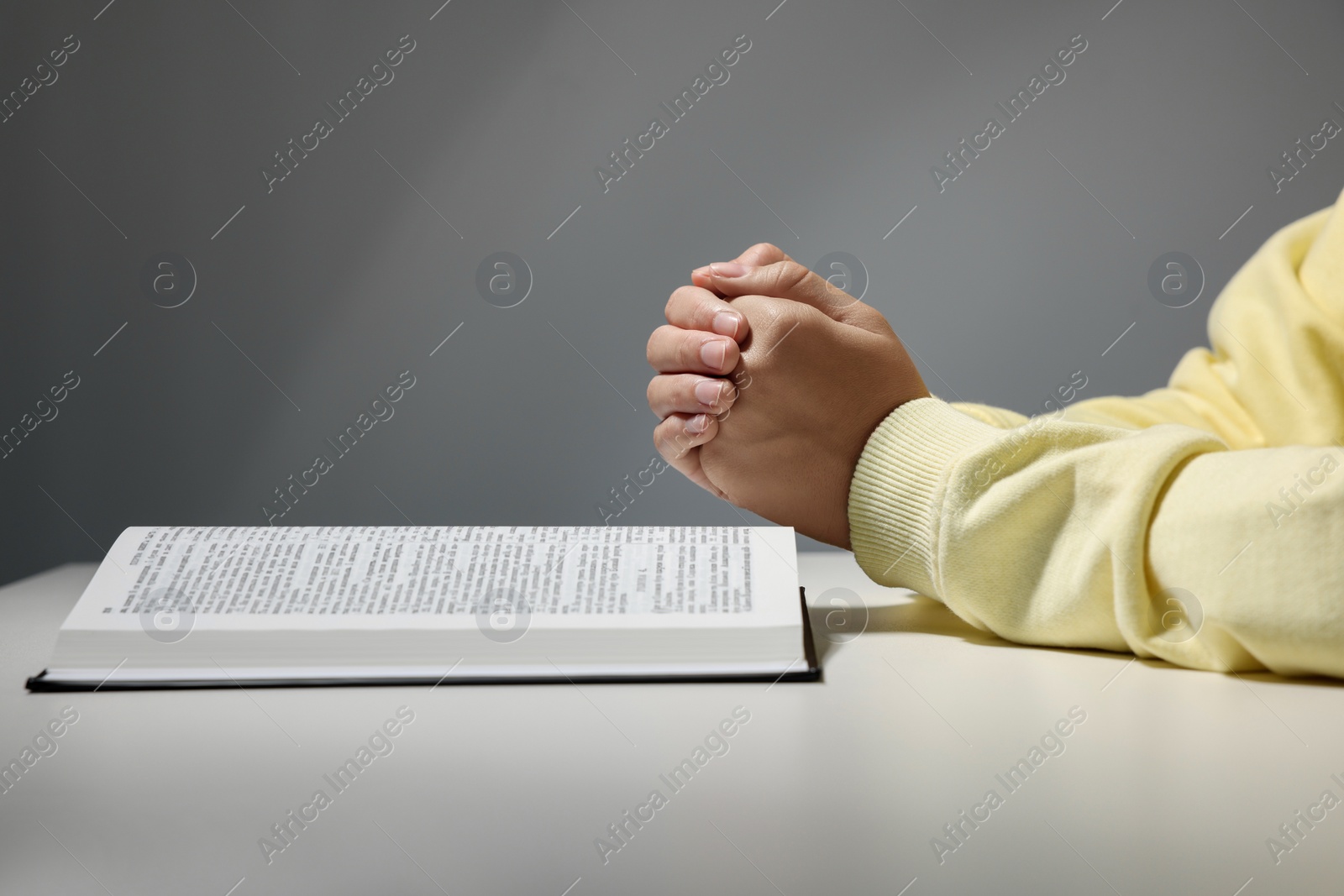 Photo of Woman praying over Bible at white table against grey background, closeup