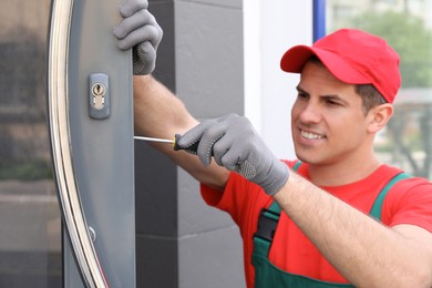 Photo of Handyman with screwdriver repairing door lock outdoors