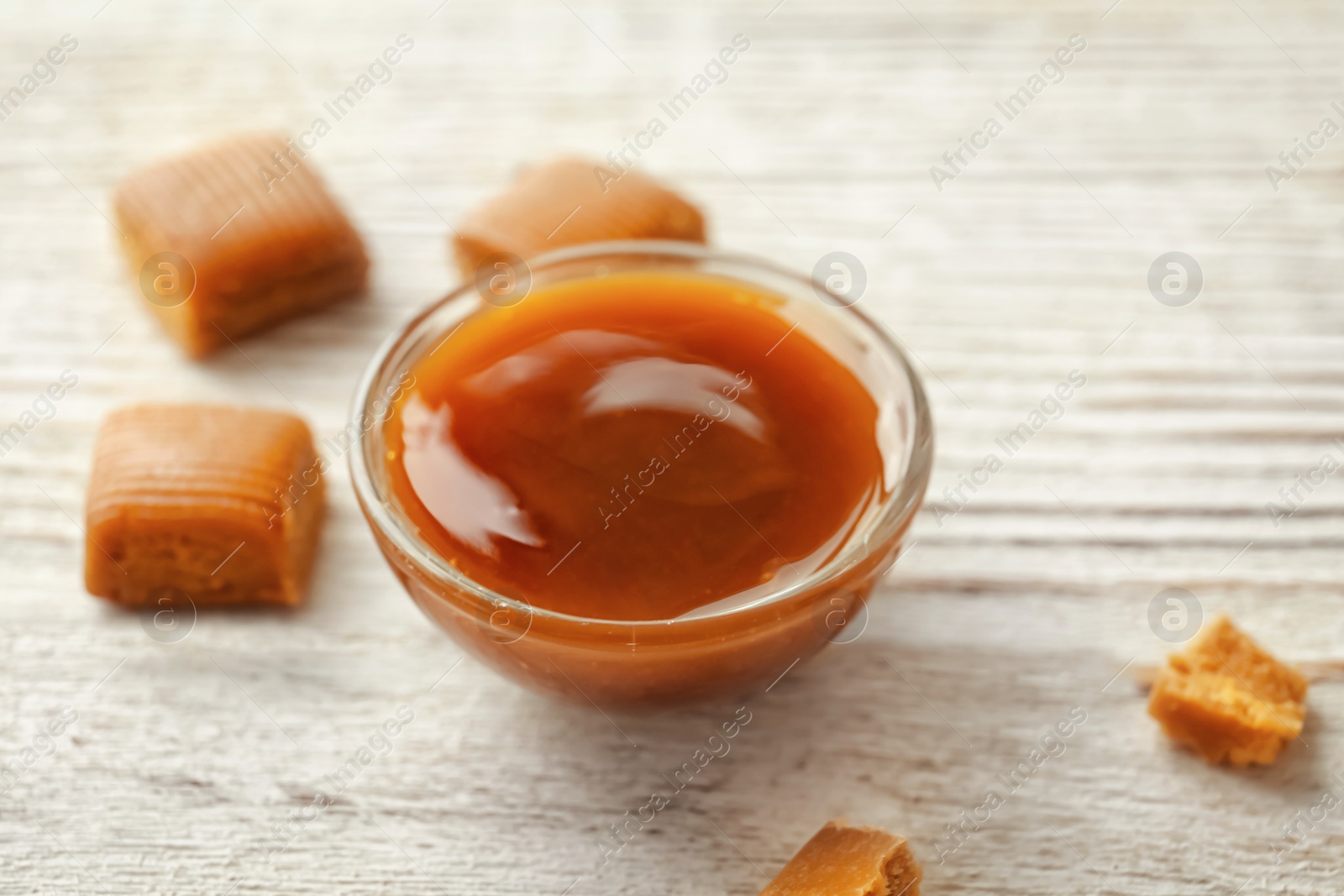 Photo of Delicious caramel candies and sauce on wooden background