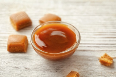 Photo of Delicious caramel candies and sauce on wooden background