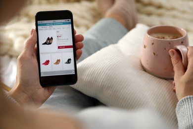 Photo of Woman with cup of coffee using smartphone for online shopping on plaid, closeup