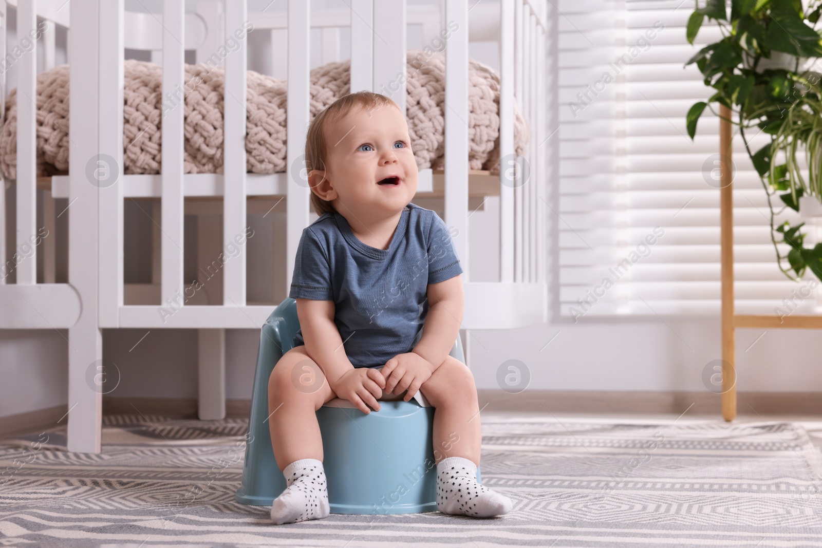 Photo of Little child sitting on plastic baby potty indoors. Space for text